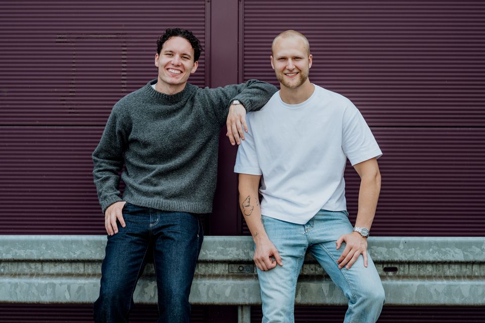 Jasper en Pim, de oprichters van Studio JAPI, leunend tegen een paarse gevel en lachend naar de camera
