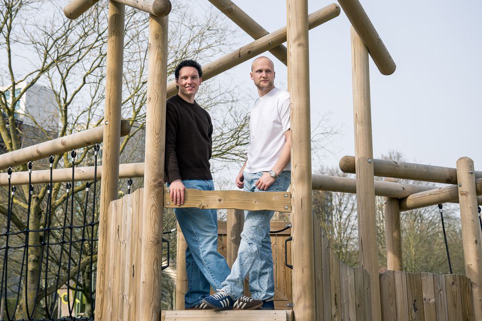 Jasper en Pim van Studio JAPI staan op een houten speeltuinconstructie in een park