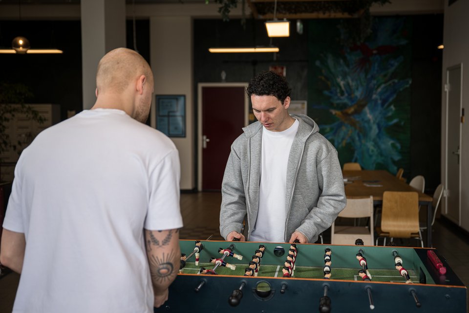 Jasper en Pim van Studio JAPI spelen tafelvoetbal op kantoor, Jasper kijkt geconcentreerd naar de bal terwijl Pim met zijn rug naar de camera staat
